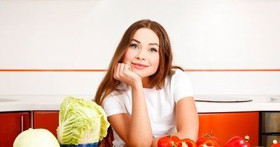 женщина посиживает за кухонным столом со свежайшими овощами